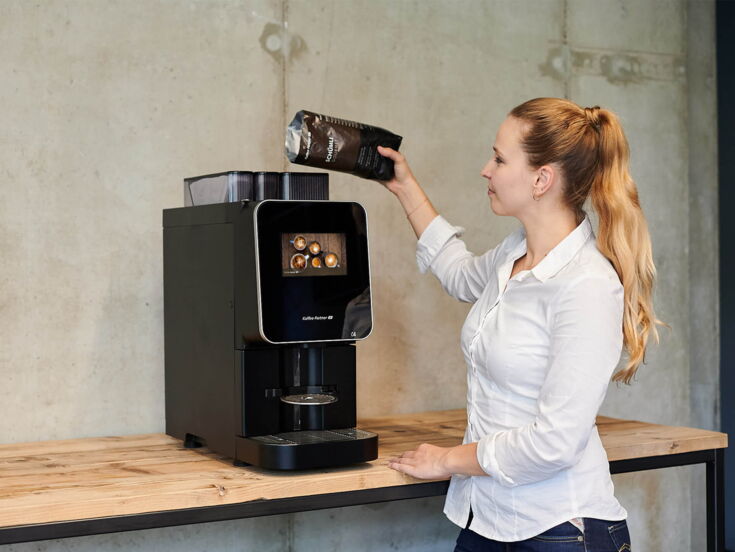 Frau füllt Kaffeebohnen in den Kaffeevollautomaten Barista Select