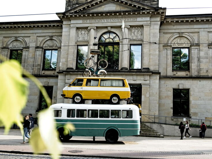 Skulptur aus gestapelten Fahrzeugen vor einem historischen Gebäude, die Kunst im öffentlichen Raum zeigt, in der Stadt Bremen