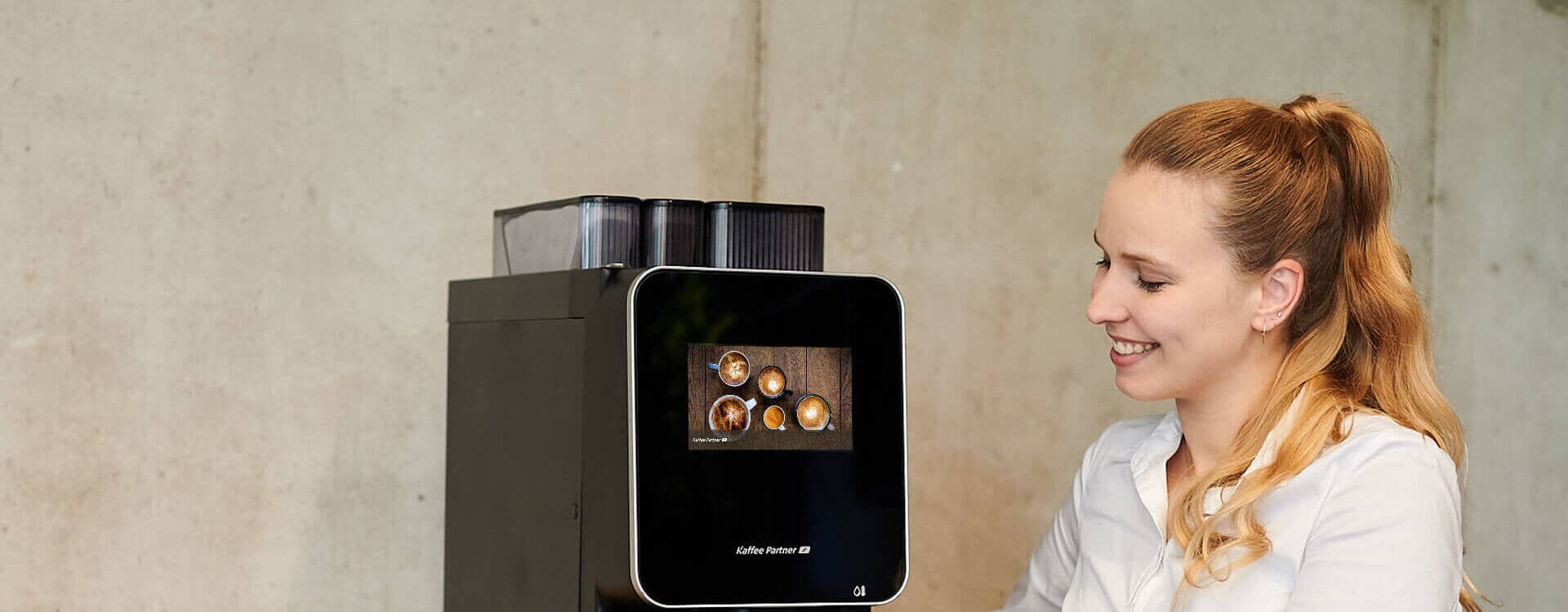 Frau möchte einen Kaffee ziehen und platziert dafür die Tasse unter der Kaffeemaschine