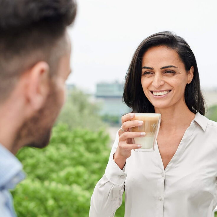 Frau trinkt Kaffee und lächelt dabei ihren Kollegen an